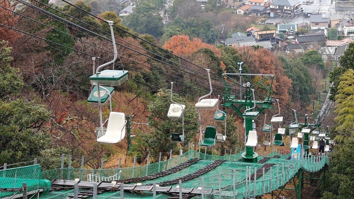 Chairlift ascending over autumn forest with distant village view