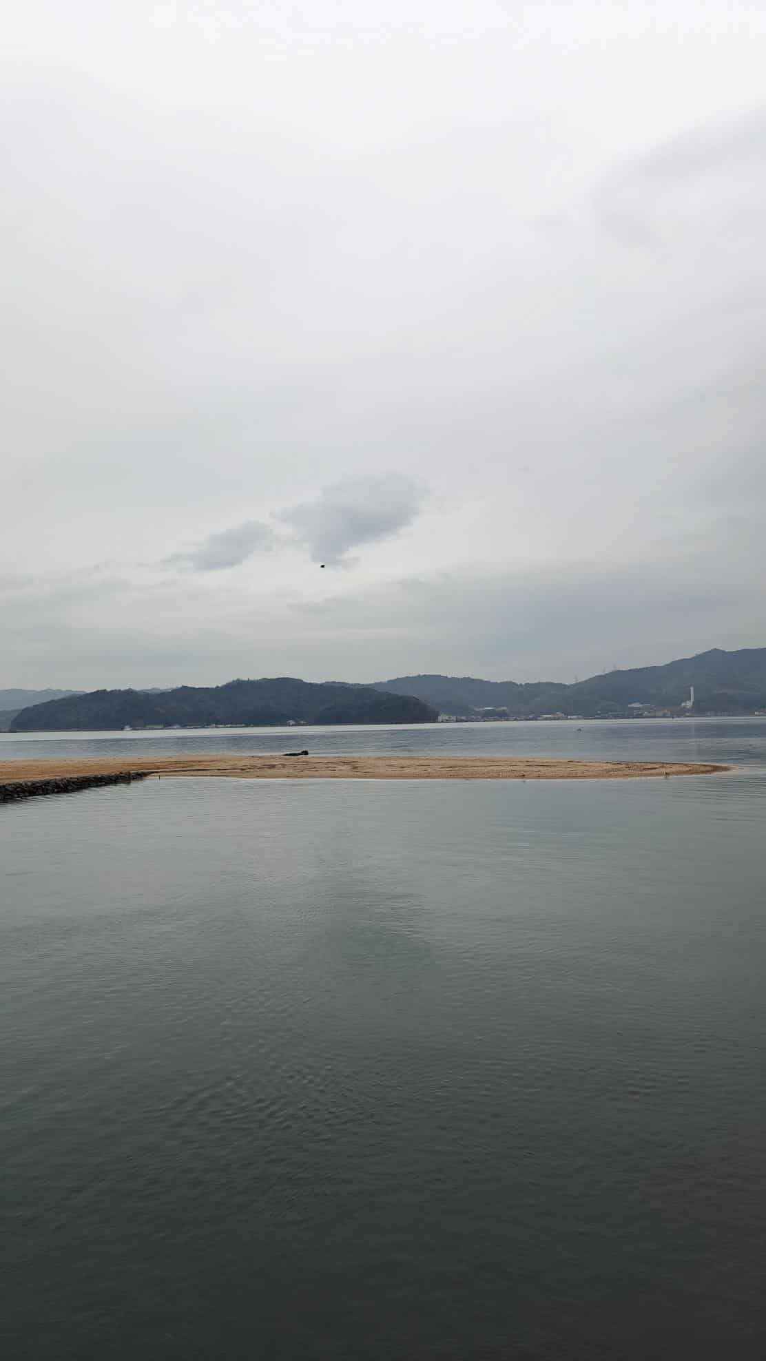 Cloudy sky over calm sea with distant hills