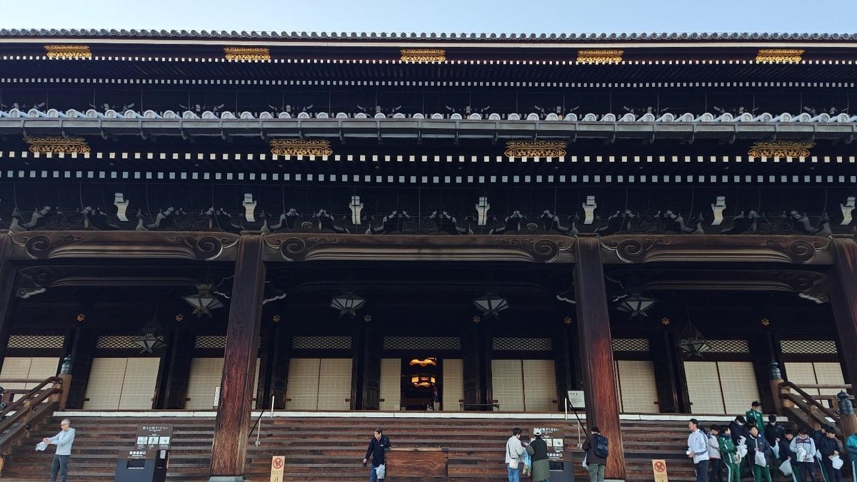 Historic wooden temple façade with visitors below in daylight.