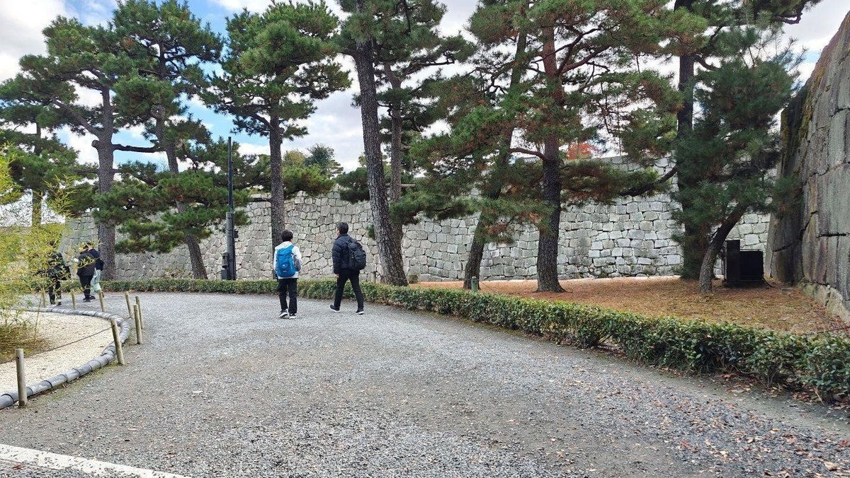 People walk near stone wall and trees