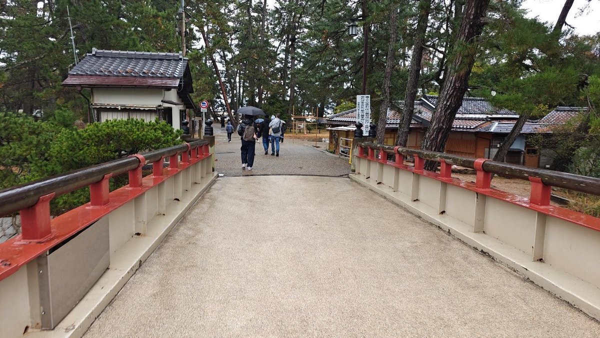 People walking on path through pine trees and traditional buildings