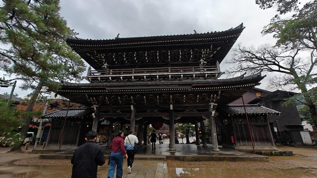 People walking towards traditional wooden gate with ornate roof