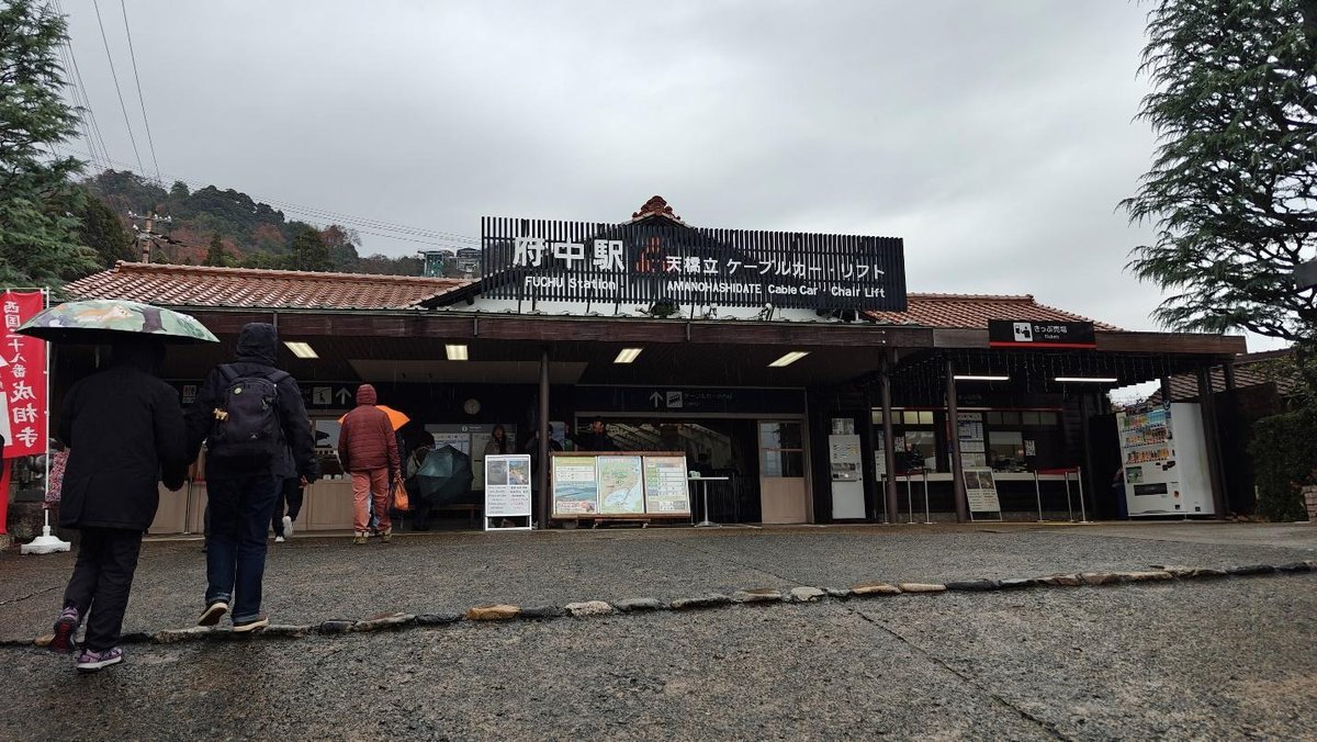 People with umbrellas entering Fuchu Station on a rainy day