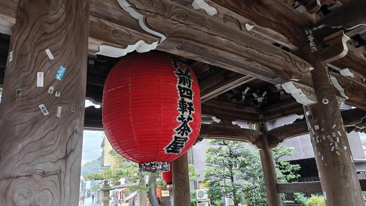 Red lantern under wooden temple structure with trees