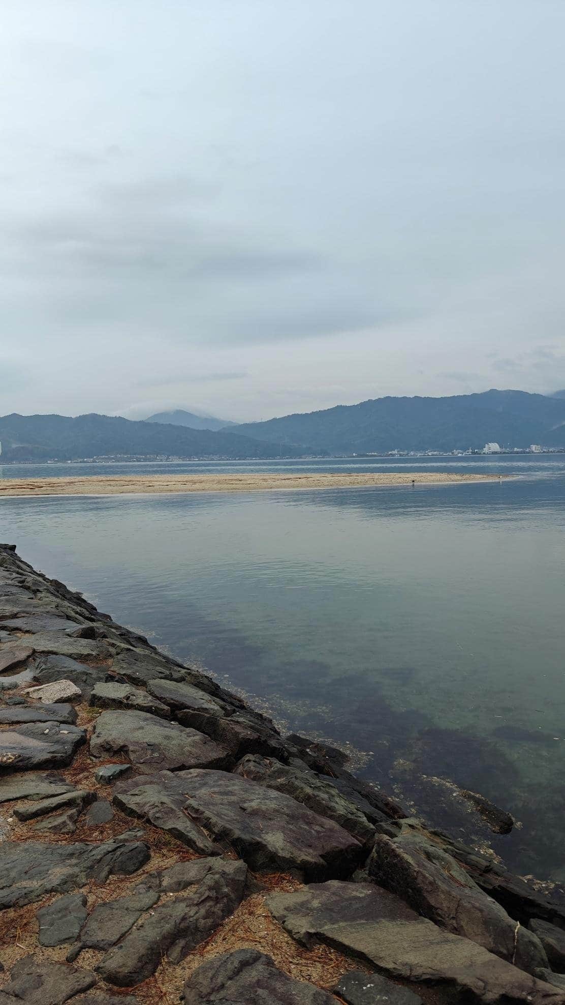 Rocky shoreline with distant mountains under cloudy sky