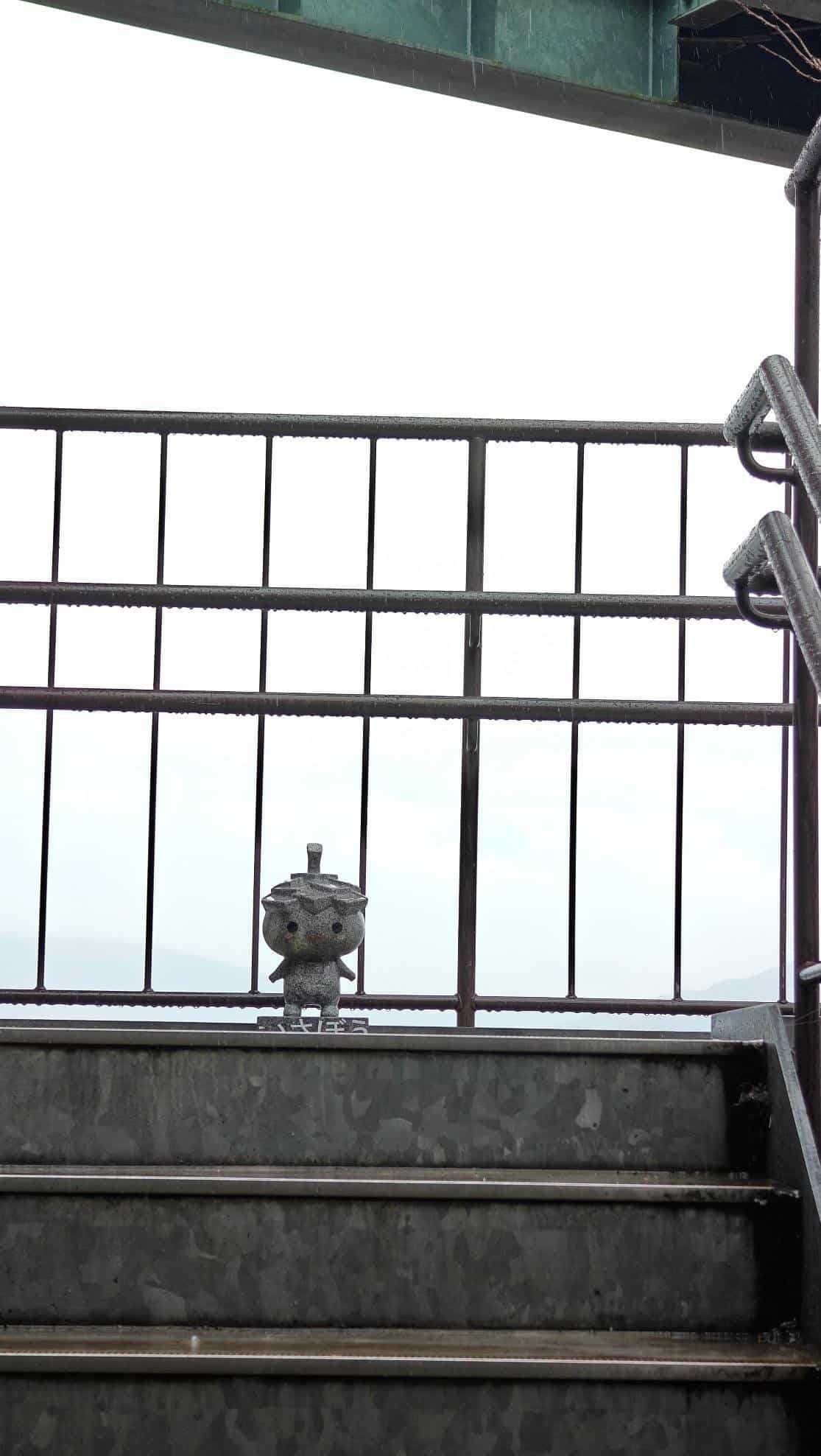 Small stone figure on metal stairs under overcast sky