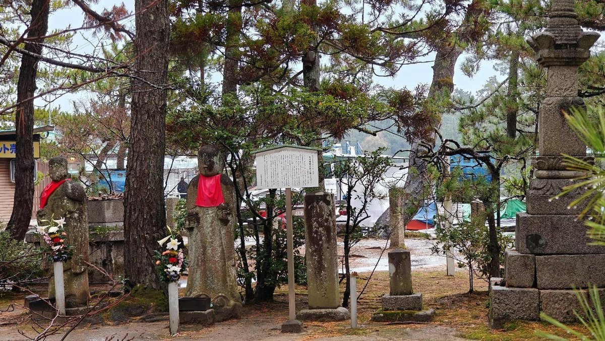Stone statues with red bibs surrounded by trees and flowers