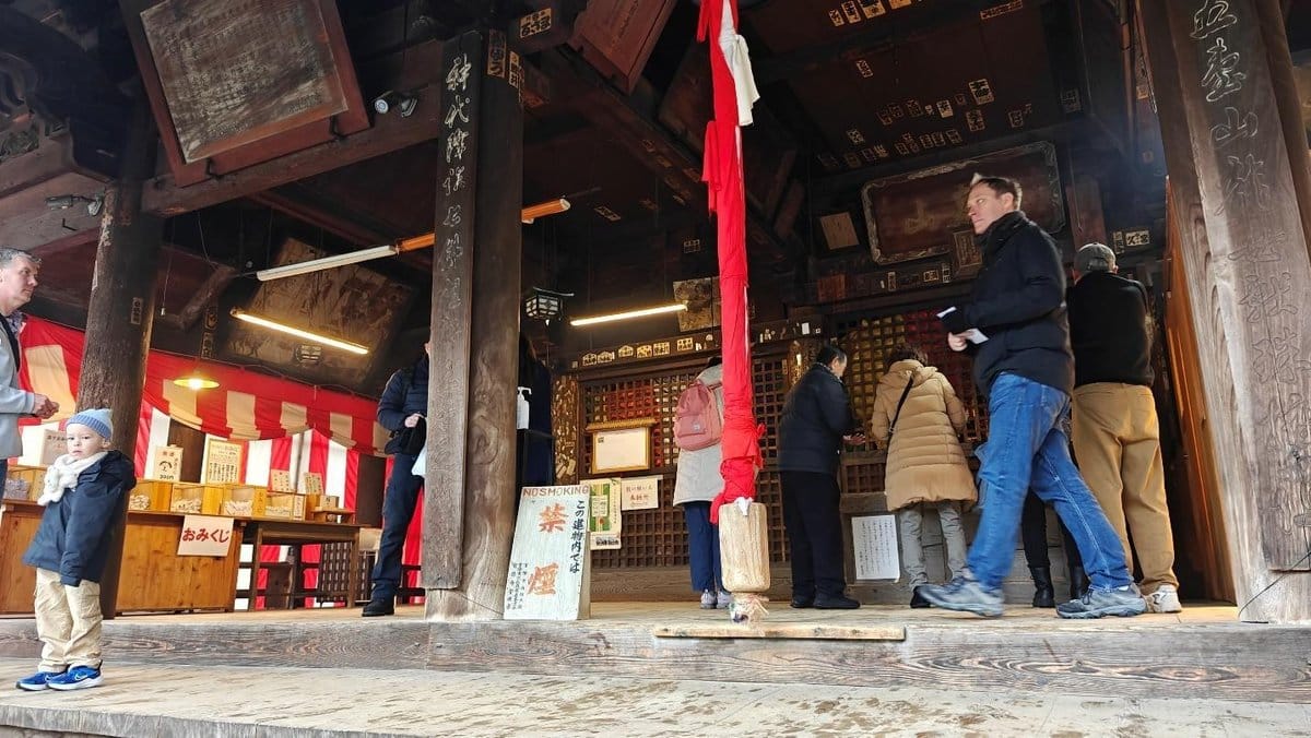 Visitors at a traditional wooden shrine with red and white banners