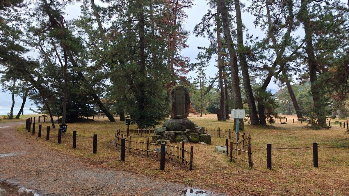 Wooded park with a stone monument and surrounding fence