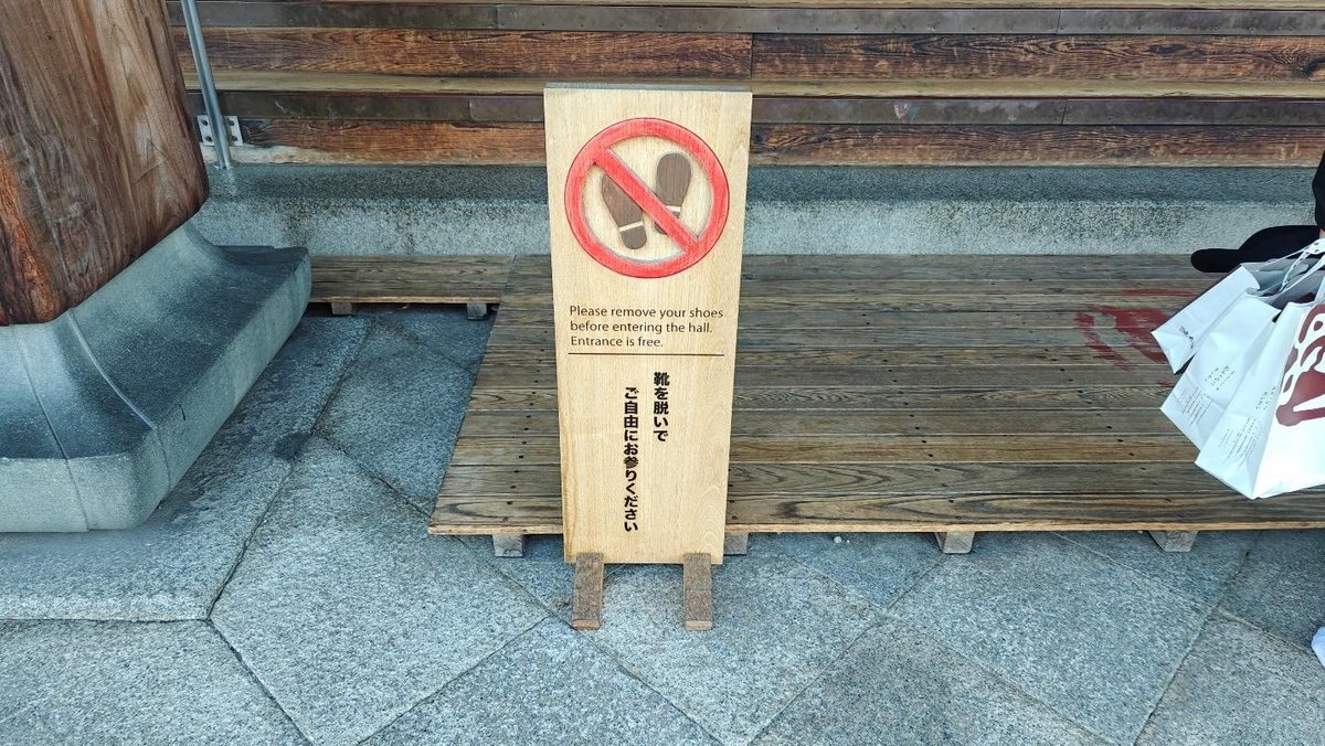 Wooden sign advising shoe removal on stone path