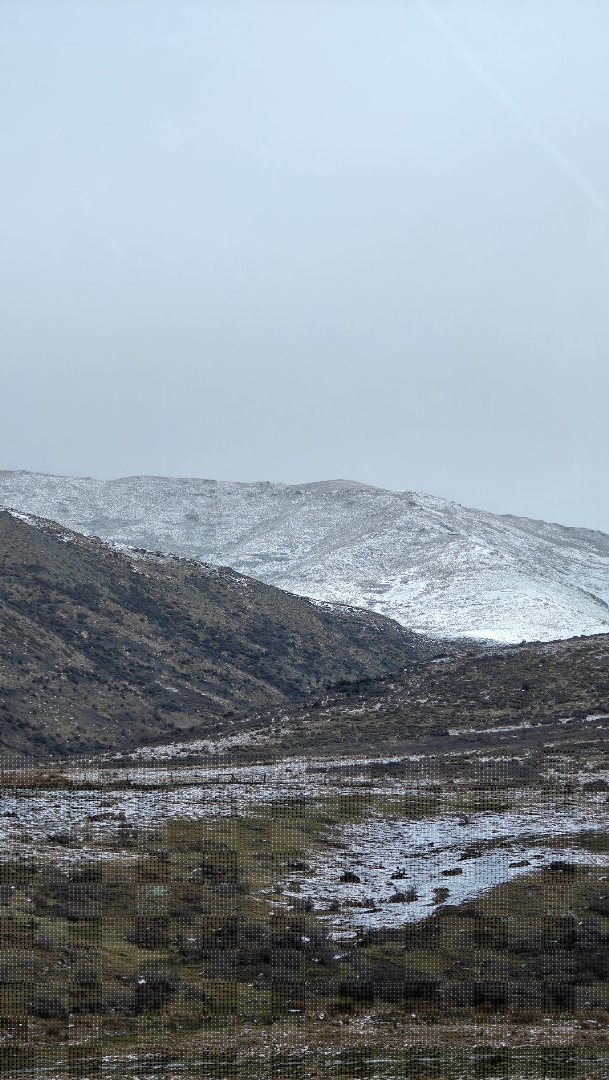 Broad snow-dusted valley of brown hills and tussock