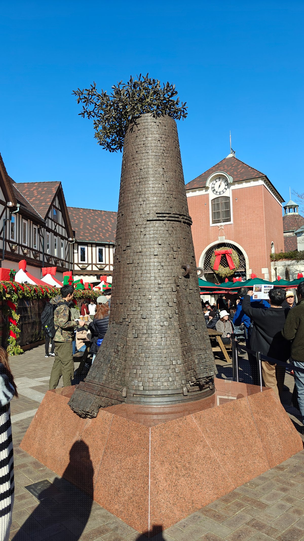Bronze conical sculpture topped with plants, market behind