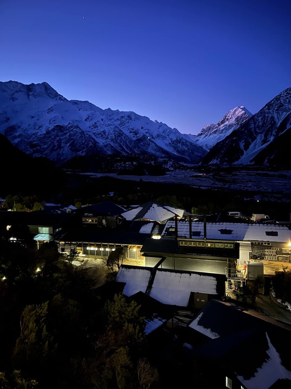 Deep-blue-hour mountains rising above the village lights (vertical).