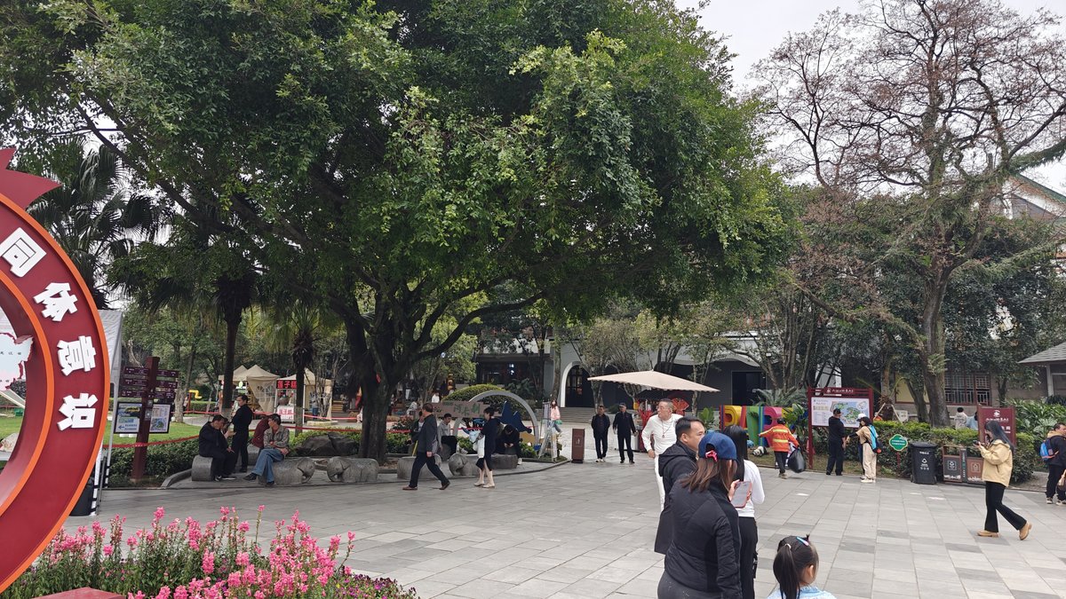 Park grounds with large trees, visitors walking, red