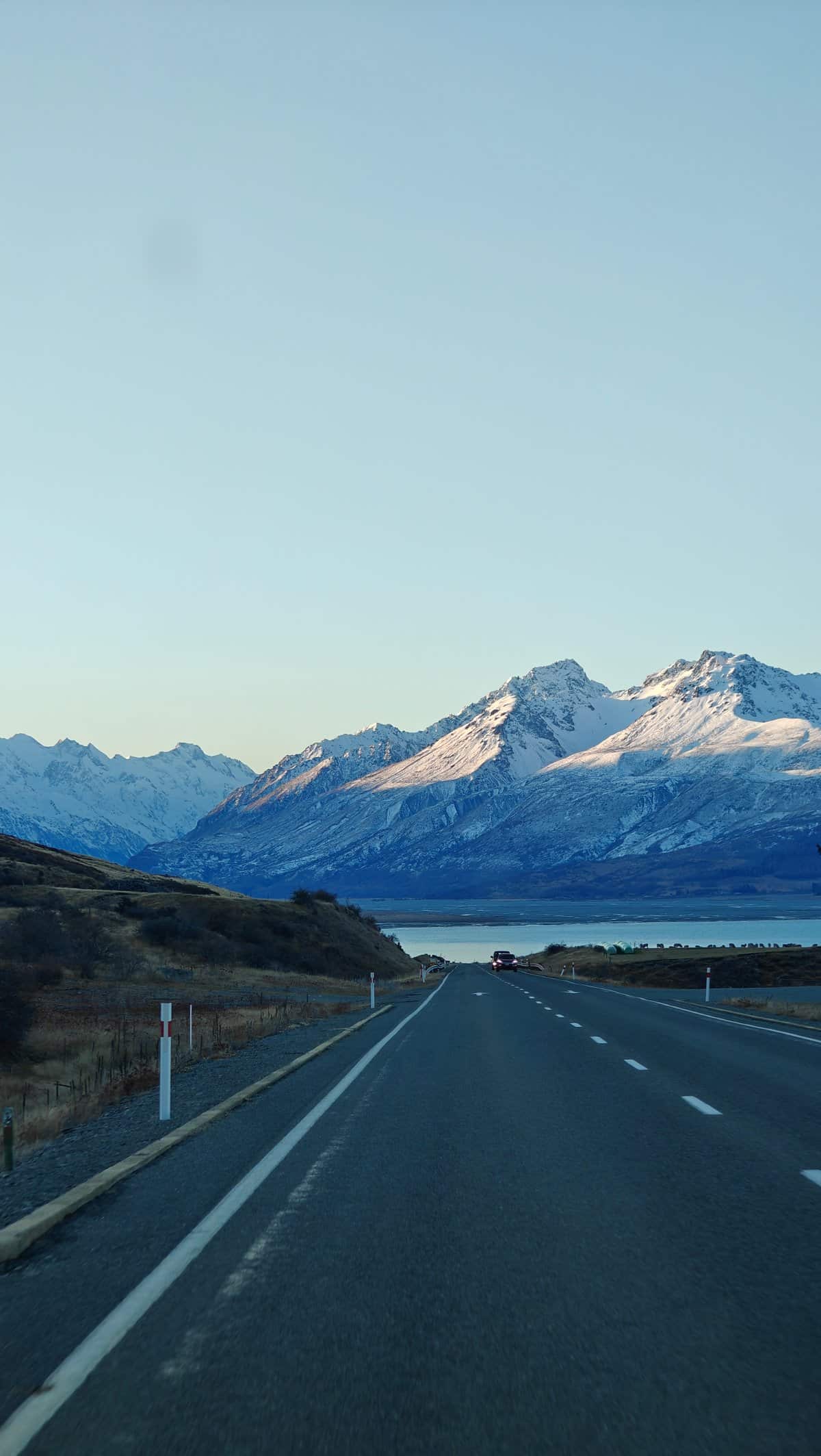 Road descending toward snow peaks and a lake