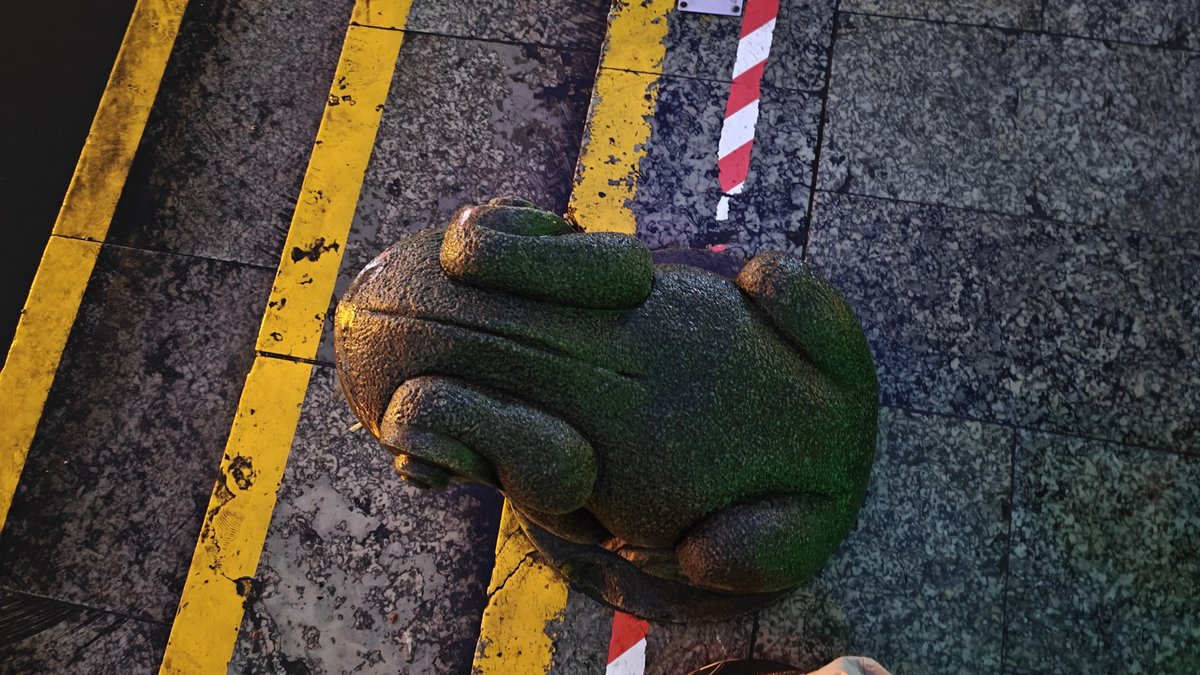 Stone frog sculpture on wet pavement with yellow