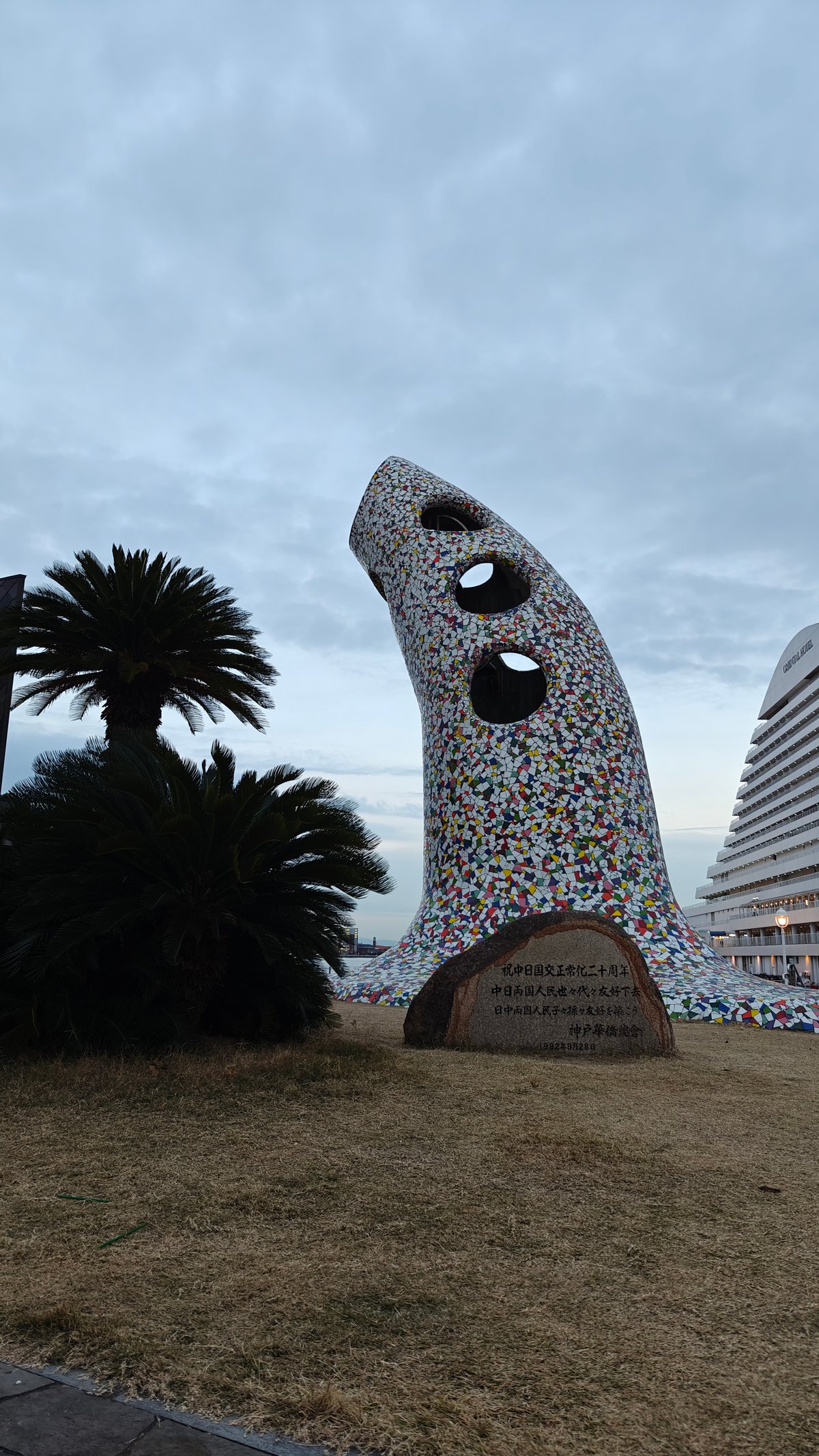 Tall colourful mosaic-tiled sculpture with a granite plaque