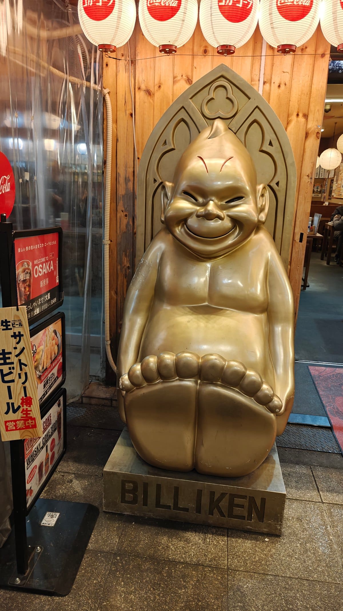 Golden Billiken statue sitting outside restaurant entrance with