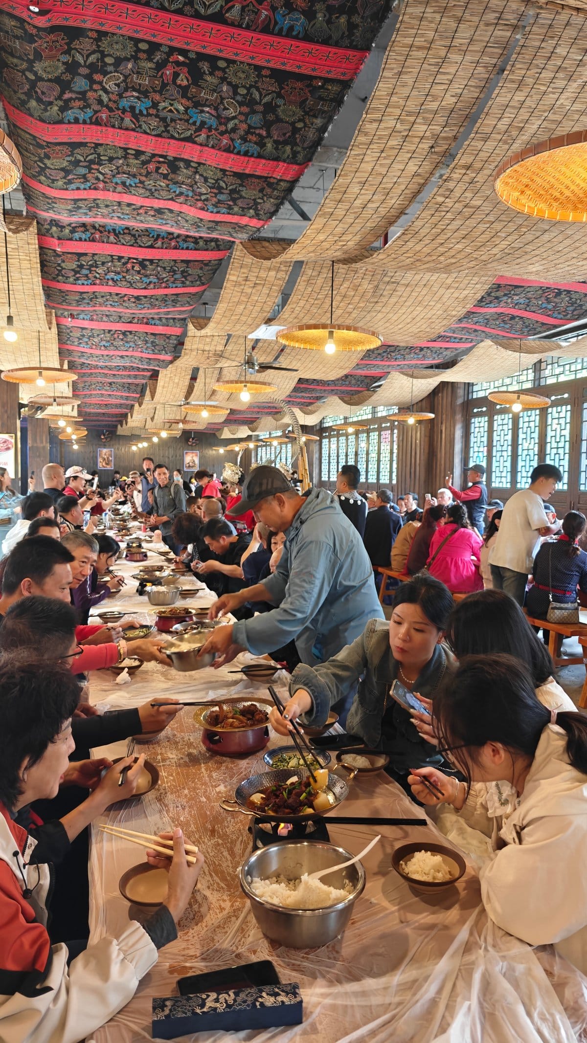The long-table dining hall down the aisle, diners
