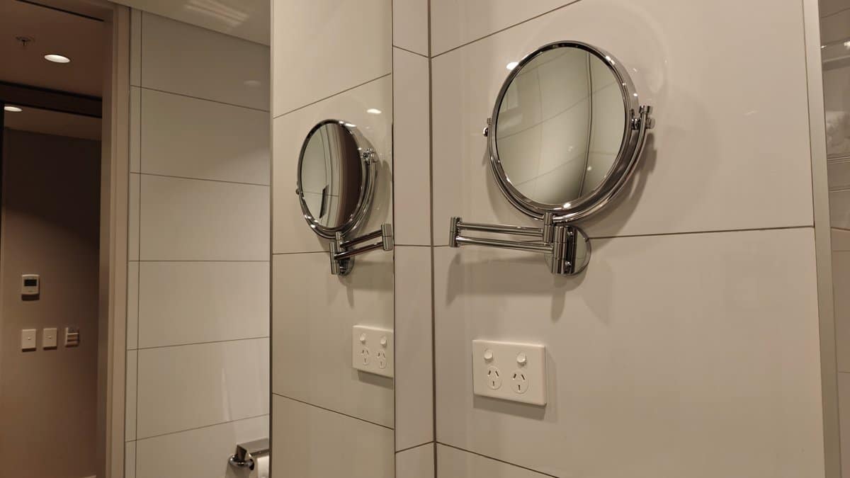A magnifying shaving mirror mounted on the tiled