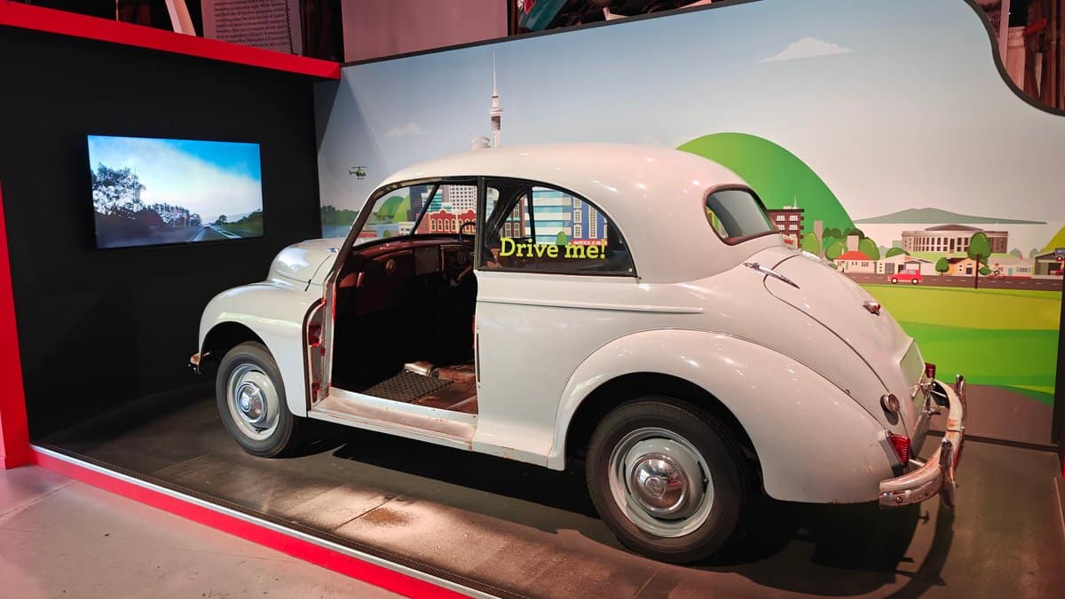 A pale Morris Minor with a Drive me!