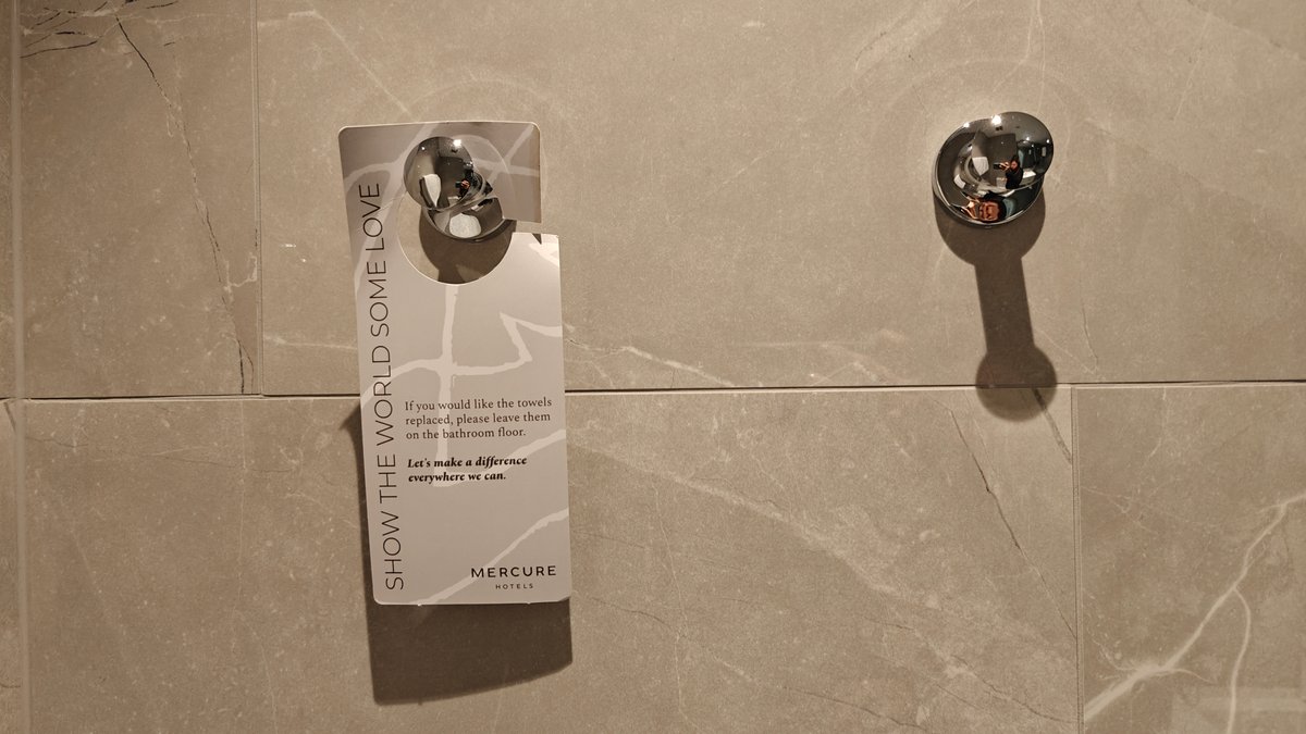 A printed linen-reuse card hanging beside the shower