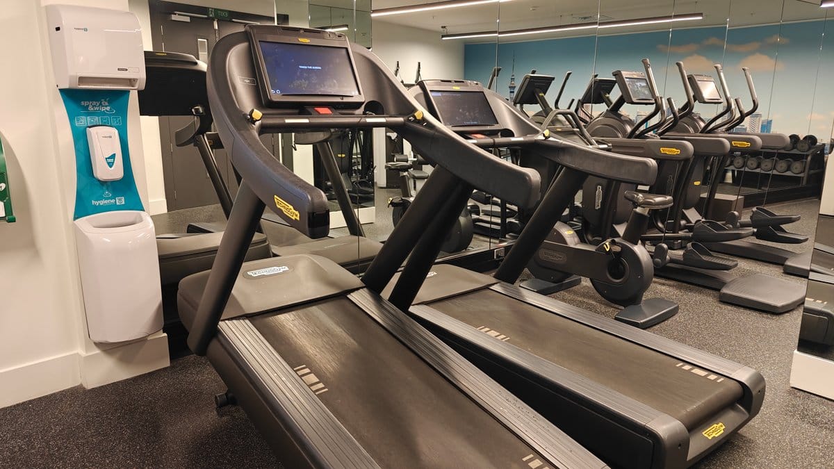 A sanitiser dispenser mounted beside the treadmill consoles.