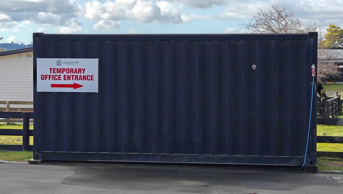 A shipping container marked TEMPORARY OFFICE ENTRANCE with