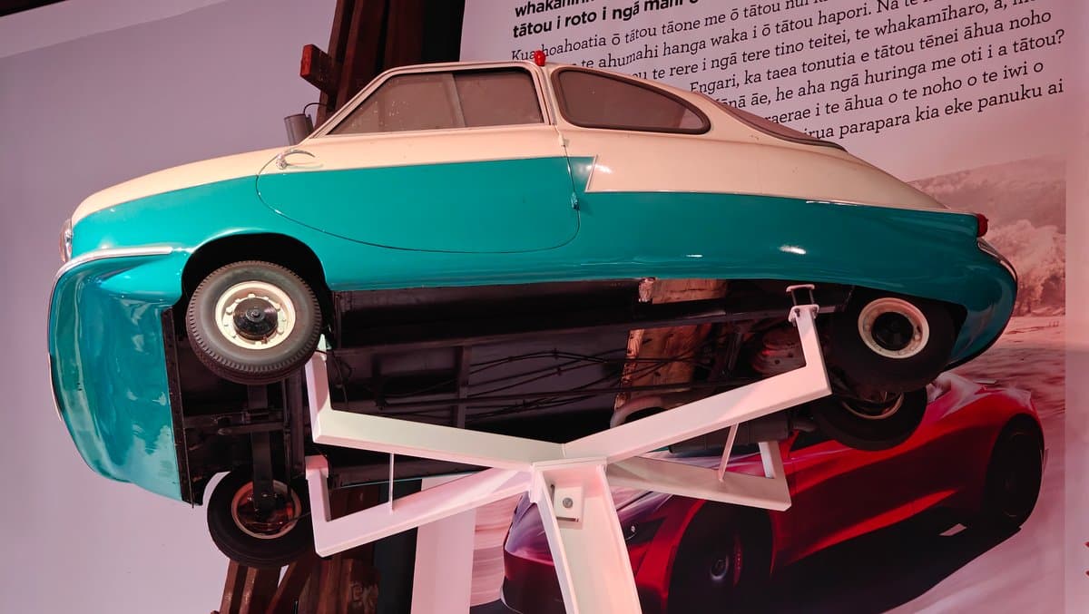 A teal and white microcar tipped on its