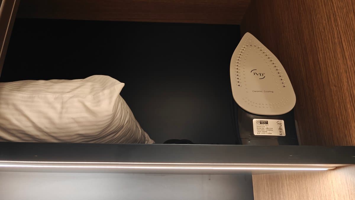 An iron and pillows stowed on the shelf